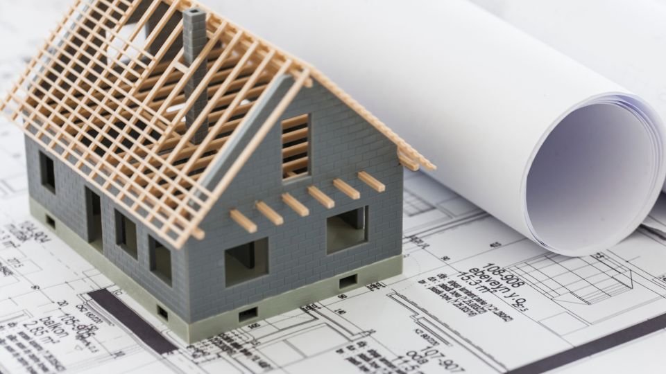 Modèle de maison sur des plans architecturaux Un modèle réduit de maison avec une charpente en bois sur des plans architecturaux et des rouleaux de papier à dessin.