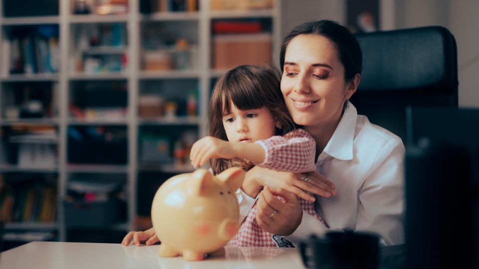Éducation financière Une mère et sa fille mettant de l'argent dans une tirelire en forme de cochon, dans un cadre familial.